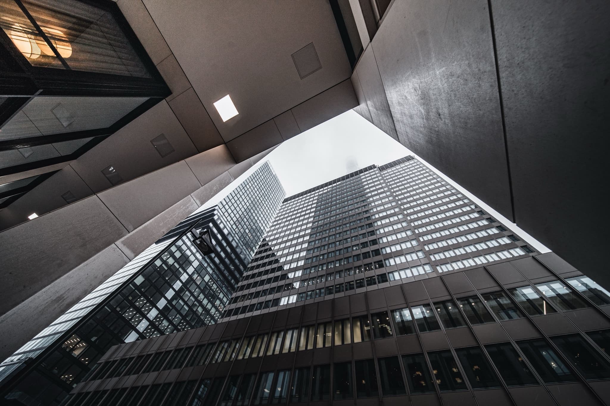 Upward view between glass office towers meeting an overcast sky